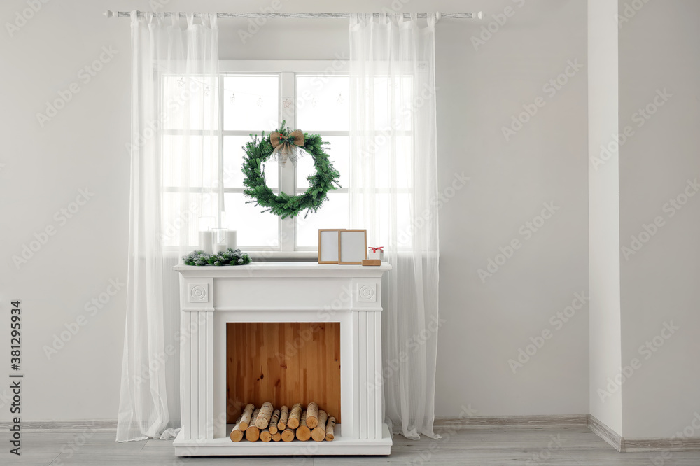 Beautiful Christmas wreath hanging on window near fireplace in room