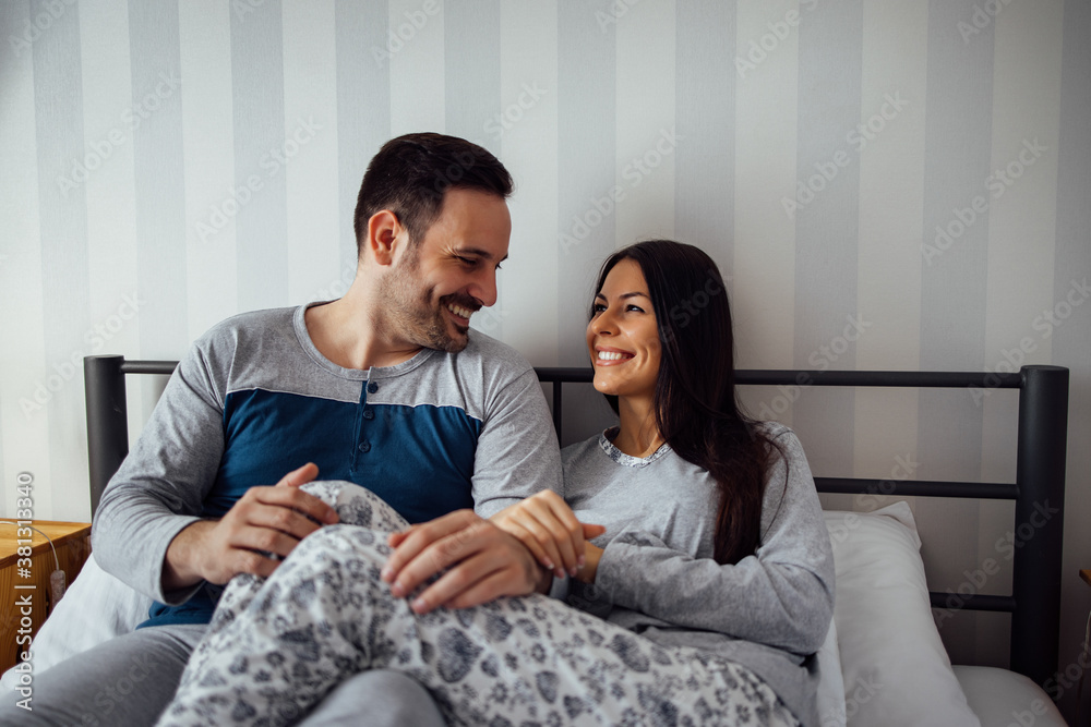 Happy couple in pajamas, sitting in bed, portrait.