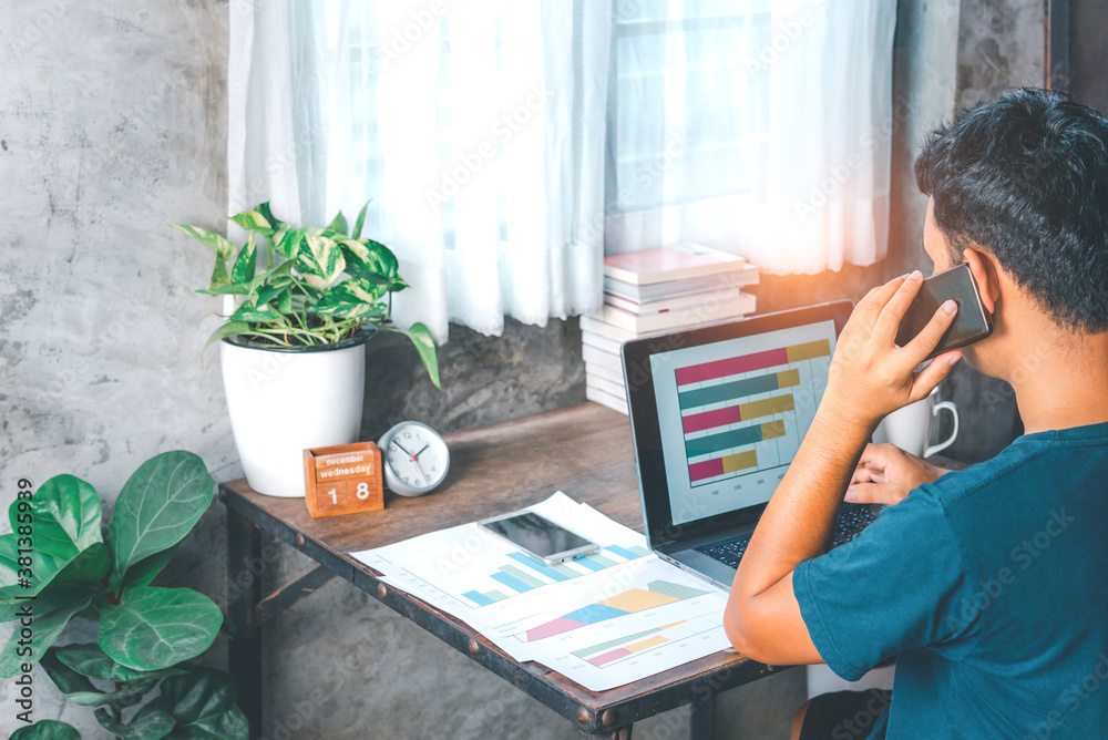 A man was working from home with a laptop ,paper sheet while making a phone call.