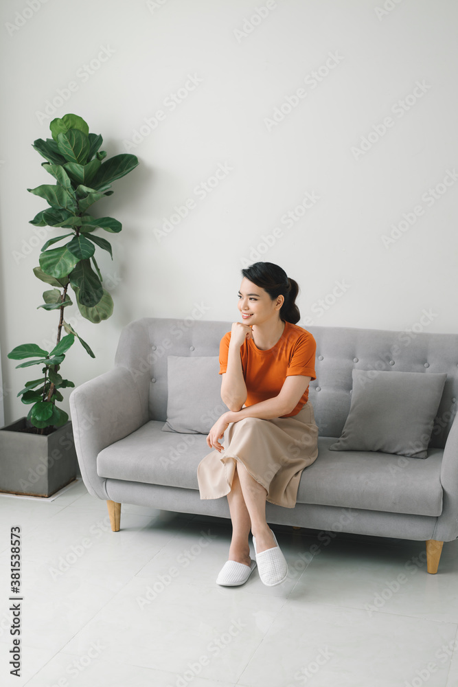 Portrait of smiling young housewife sitting on couch in living room