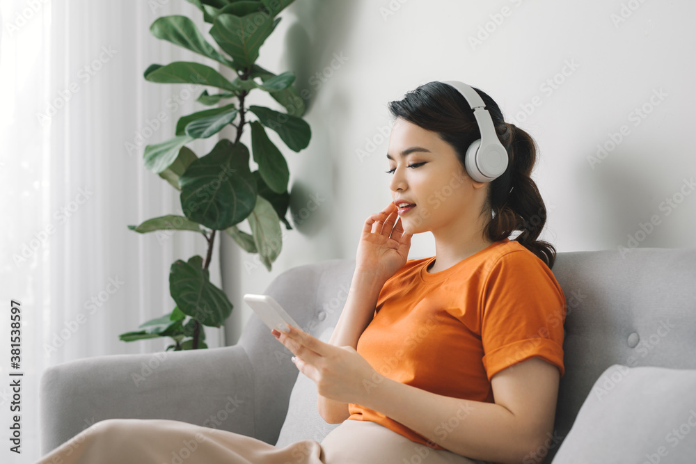 Portrait of a cheerful young woman listening to music with mobile phone while resting on a couch at 