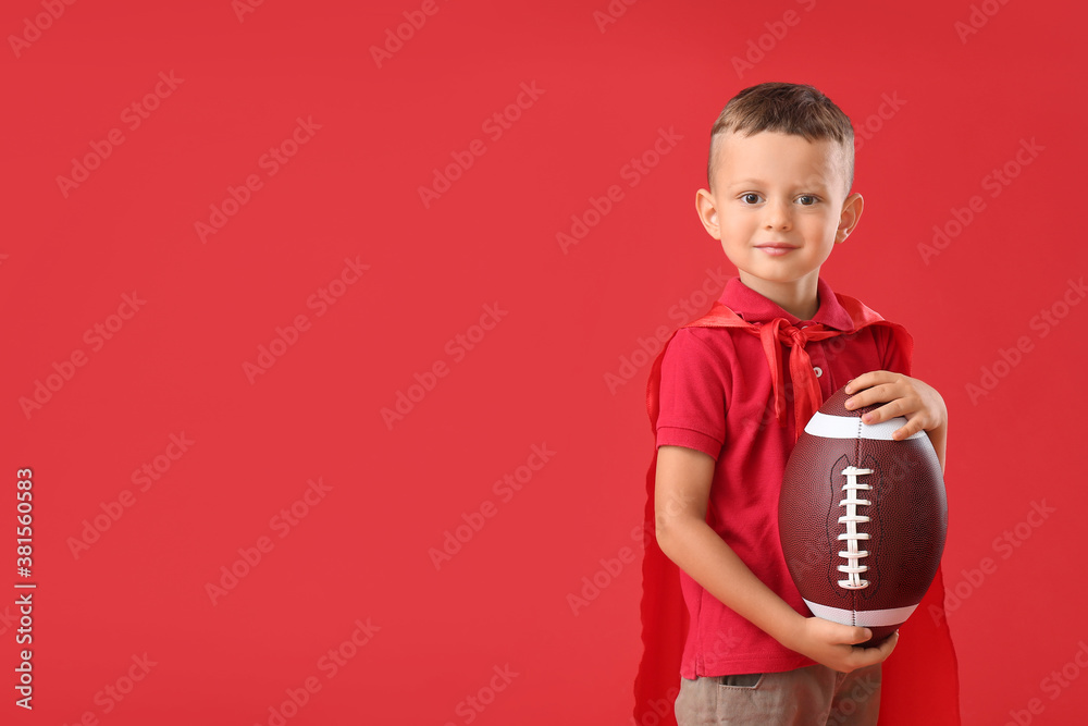 Little boy with rugby ball and cloak on color background