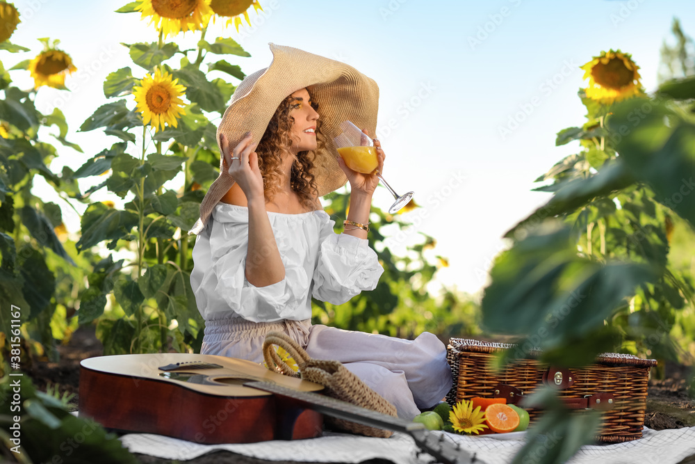 Beautiful young woman with guitar having picnic in sunflower field