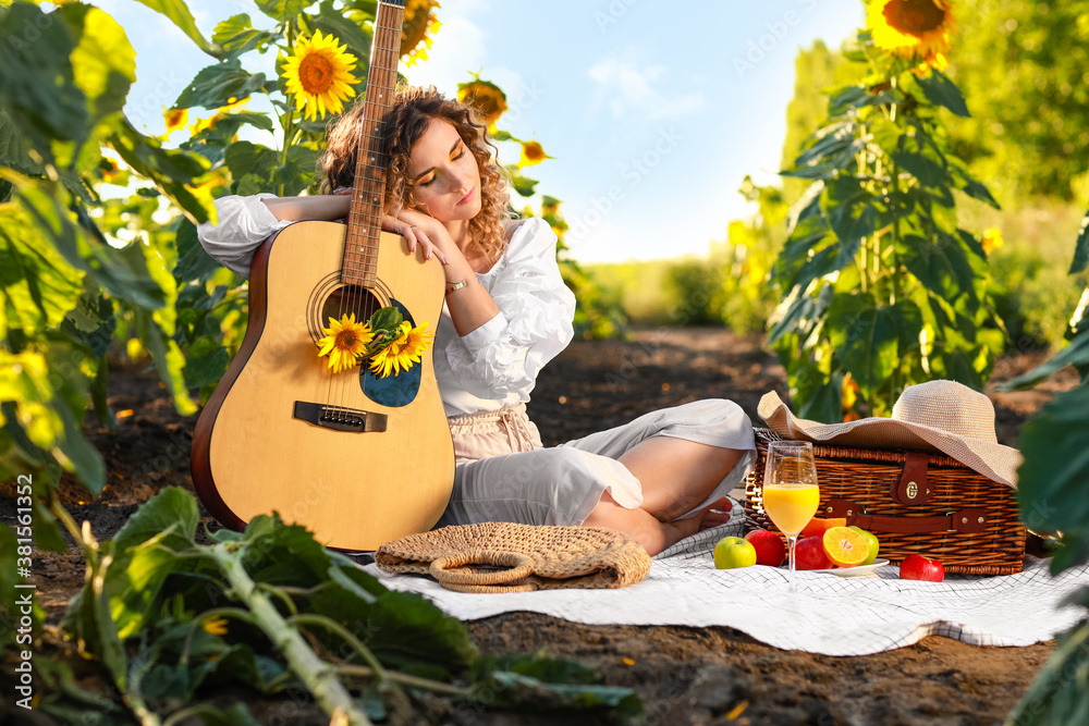 Beautiful young woman with guitar in sunflower field