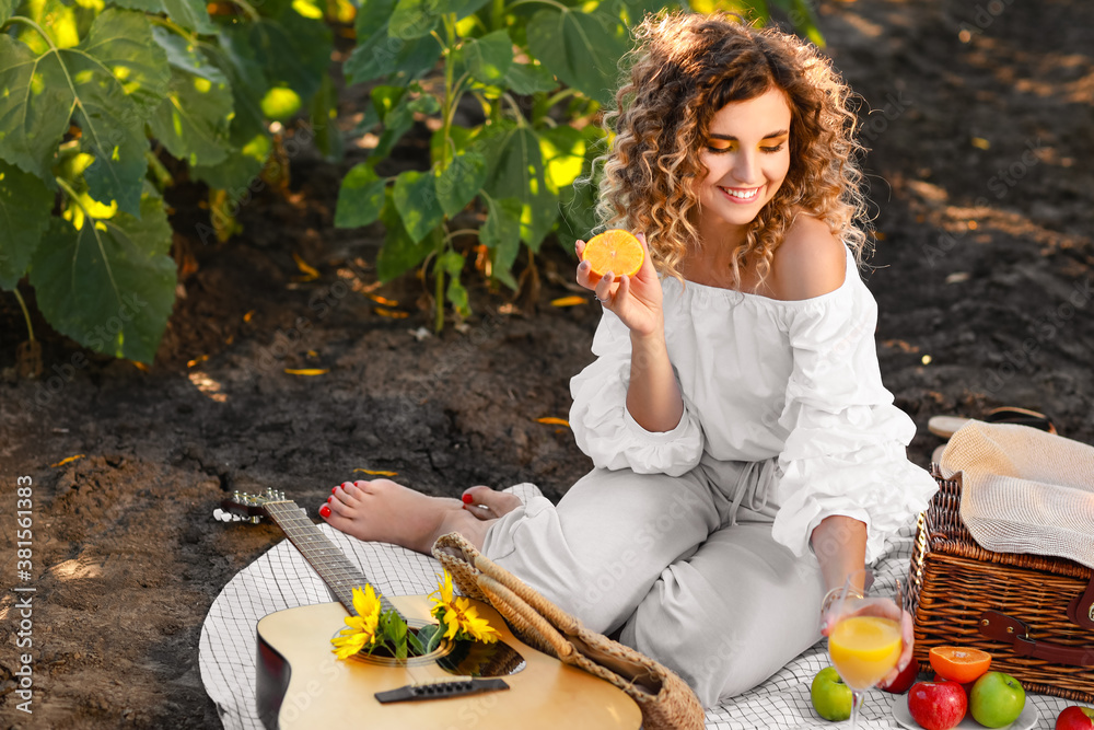 Beautiful young woman with guitar having picnic in sunflower field