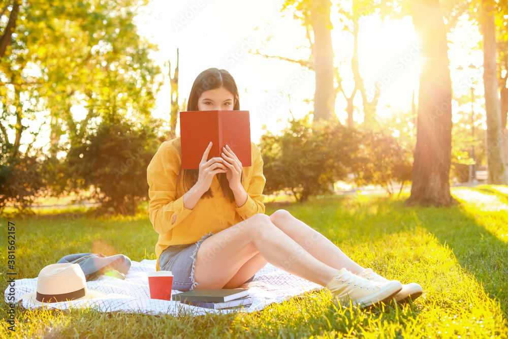 Beautiful young woman reading book in park