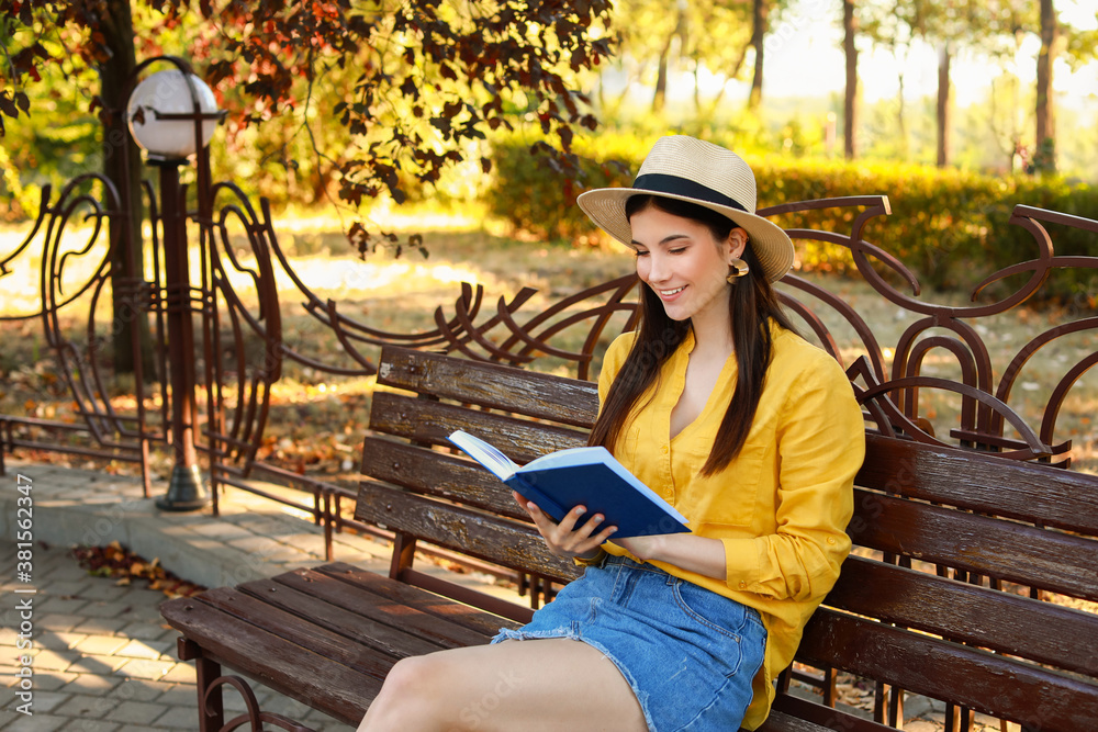 Beautiful young woman reading book in park