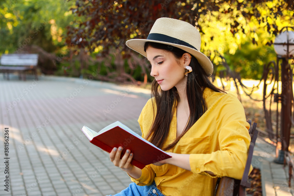 Beautiful young woman reading book in park