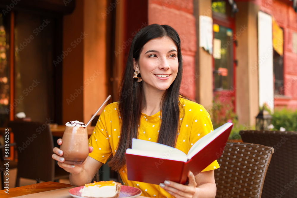 Beautiful young woman reading book in street cafe