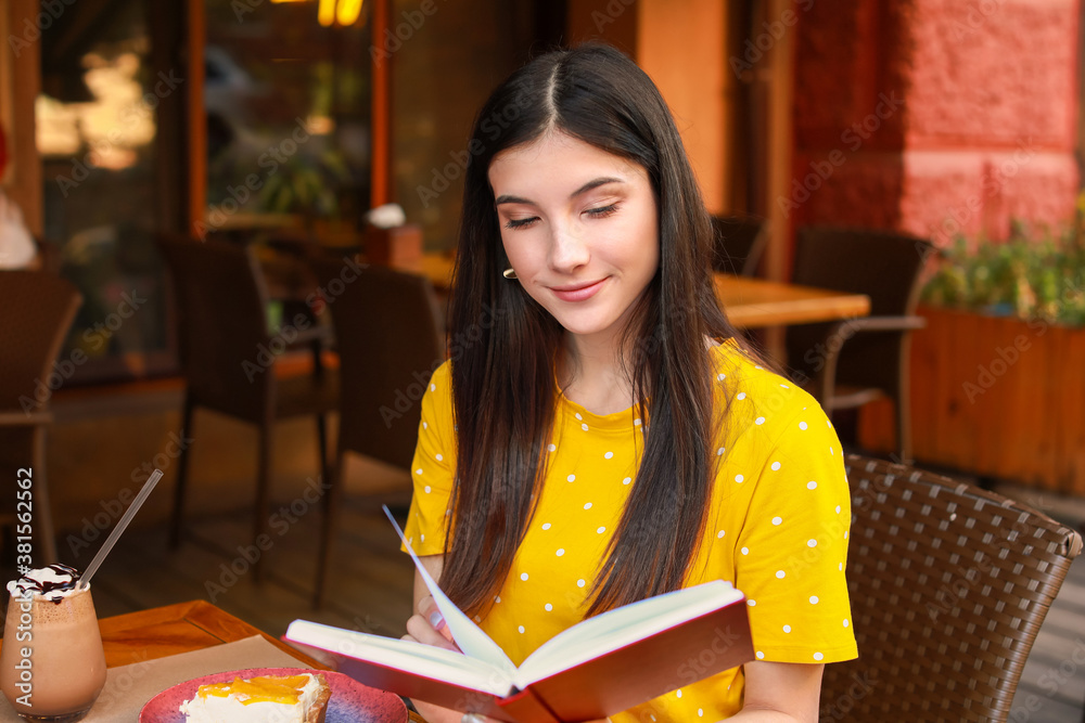 Beautiful young woman reading book in street cafe