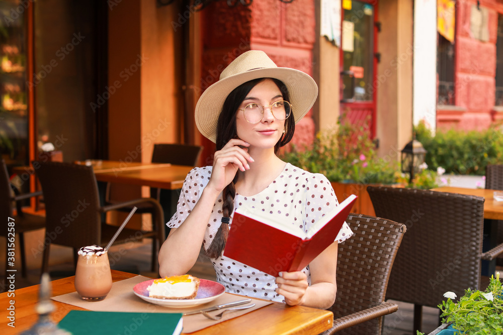 Beautiful young woman reading book in street cafe