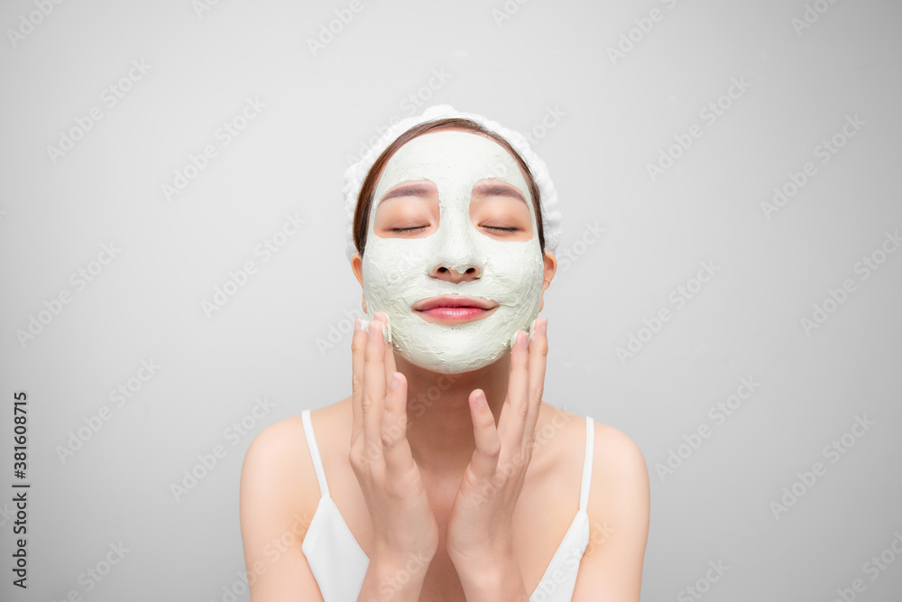 Portrait of satisfied woman improves her skin condition, wears facial mask, touches cheeks over whit