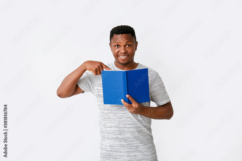 African-American man reading book on light background