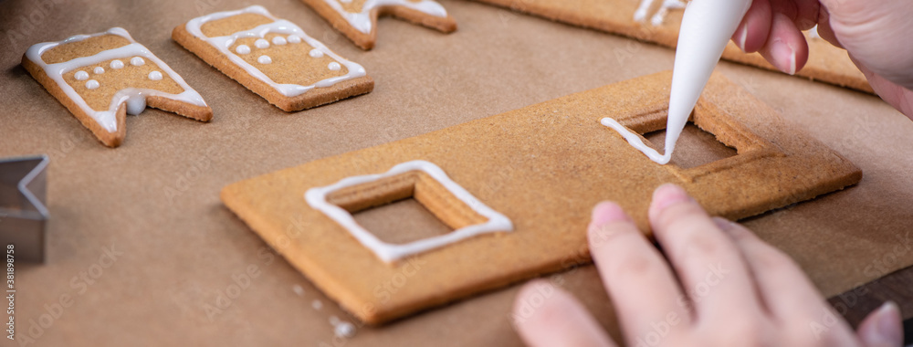 Young woman is decorating Christmas Gingerbread House cookies biscuit at home with frosting topping 