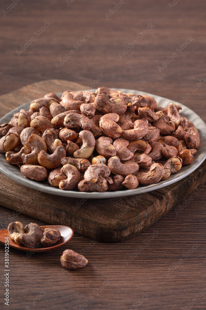 Cashew nuts with peel in a plate on wooden tray and table background, healthy raw food concept.