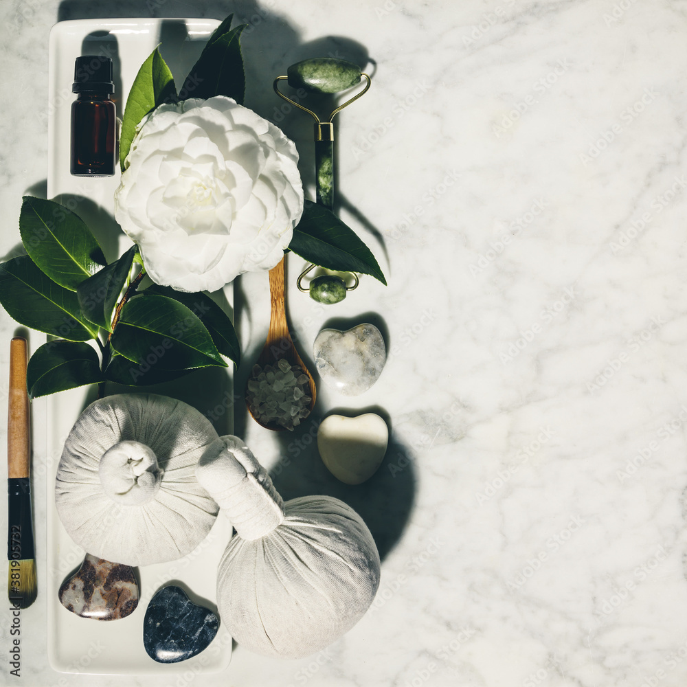 Flat lay composition with spring camelia flower and various beauty care products on white marble tab