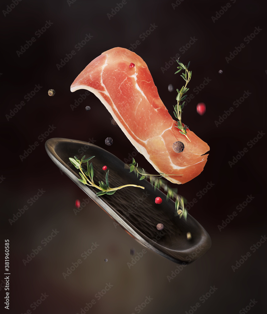 Slice of dried ham with spices in the air on a dark background