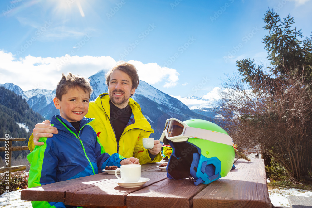 Father in ski outfit hug holding by shoulder little boy enjoy lunch break over mountain view after s