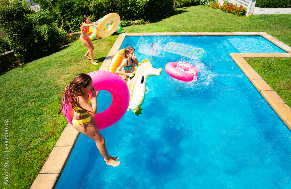 Group little kids in mid air jump into the swimming pool holding inflatable toys diving in the water