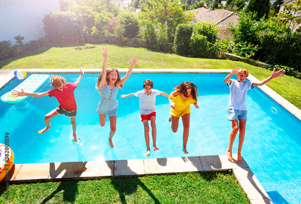 Group of happy teen children in mid air fall into pool water hands up view from above