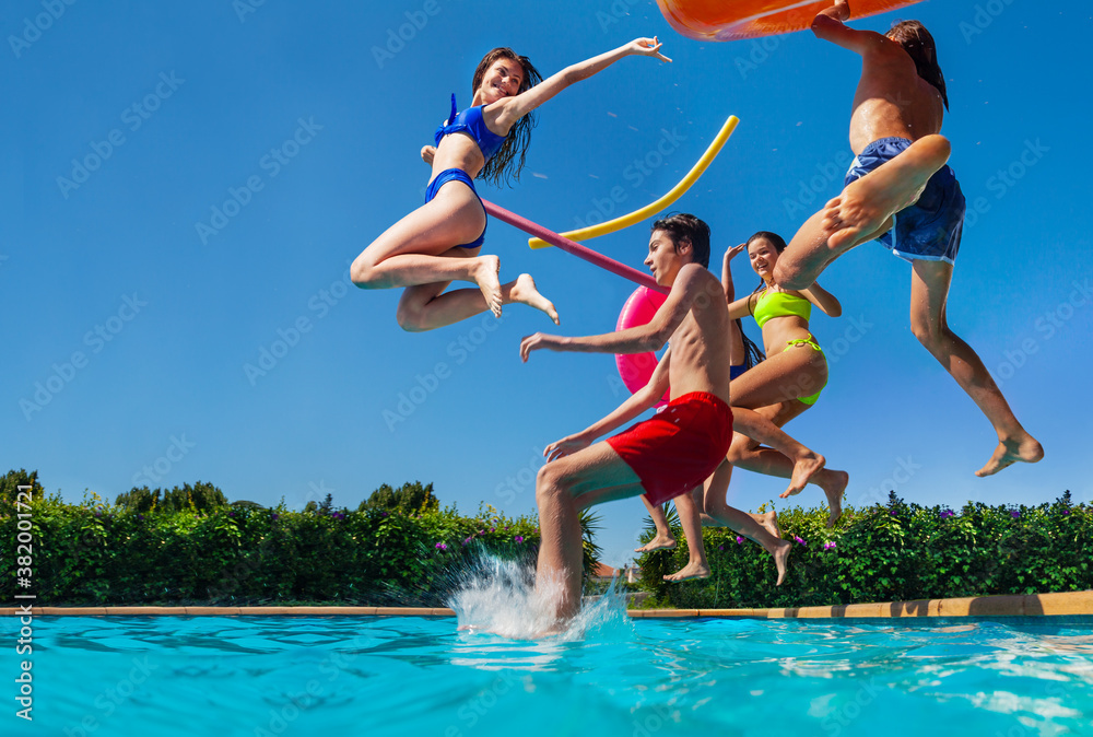 Group of happy teenage kids dive in the swimming pool water throw inflatable toys lifting hands have