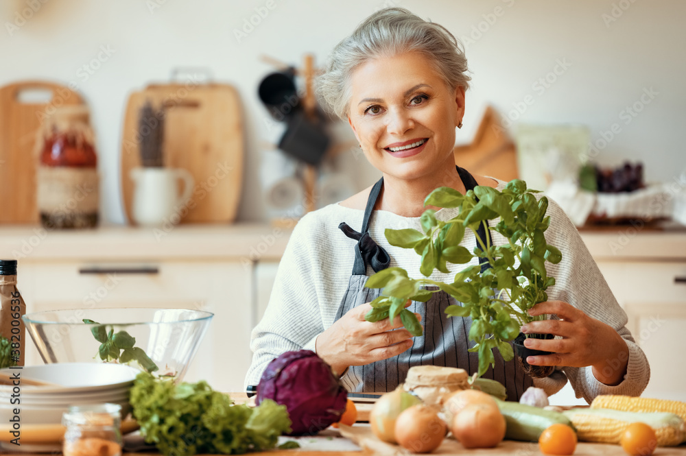 Happy mature woman preparing healthy salad in kitchen.