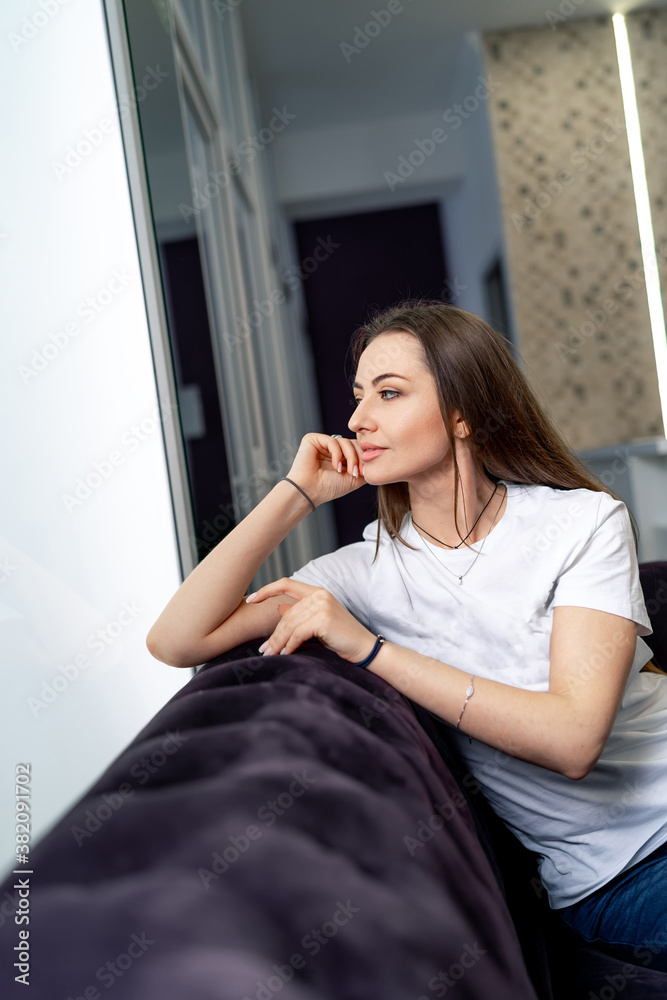 Young attractive woman relaxing on sofa. Pretty girl is posing to camera. White shirt and long hair.