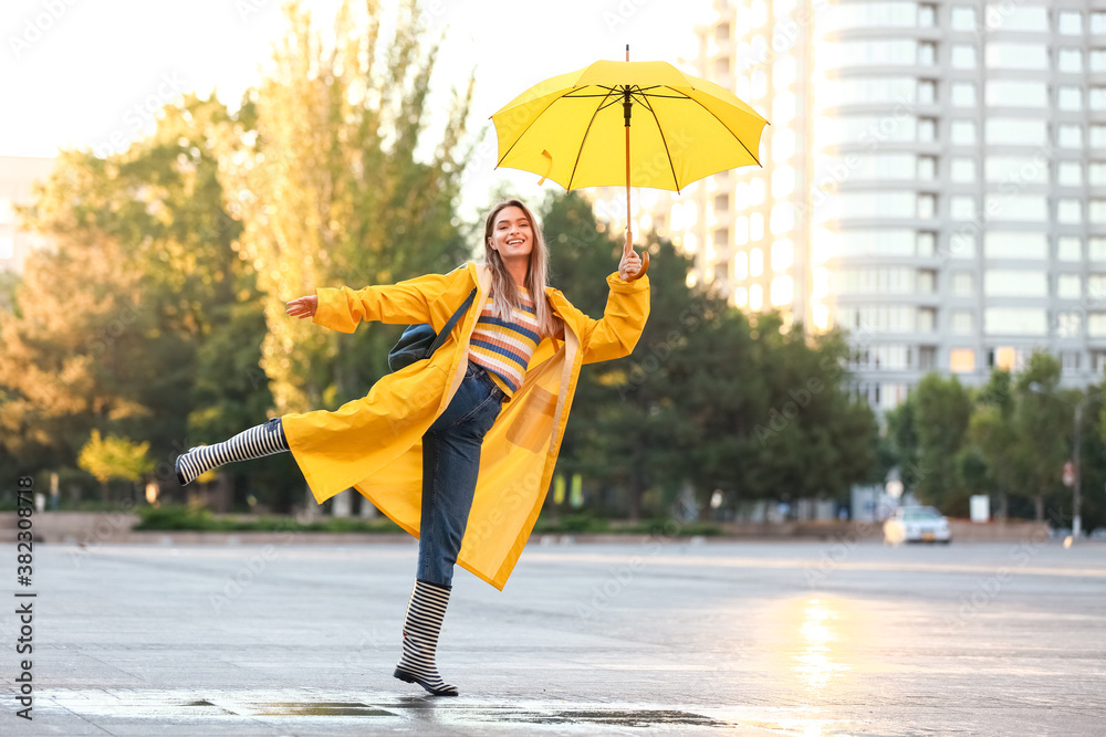 Beautiful young woman with umbrella wearing raincoat outdoors