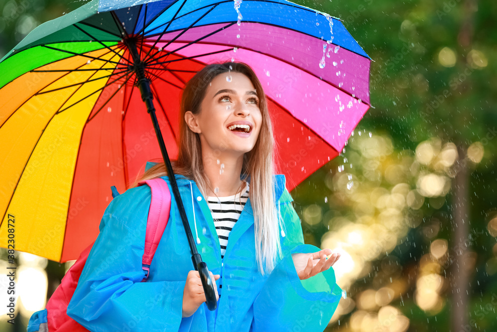 美丽的年轻女子在公园里打着雨伞，穿着雨衣