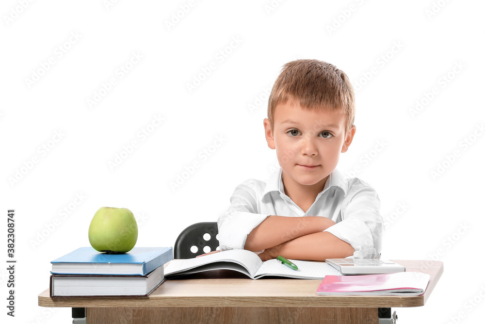 Little pupil sitting at school desk against white background