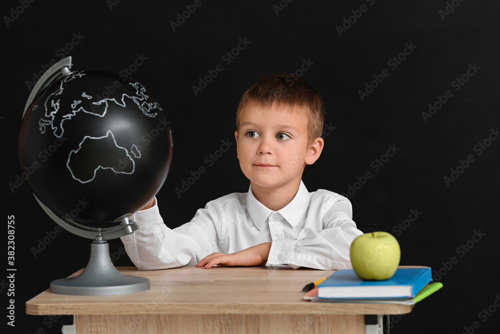 Little pupil sitting at school desk against dark background