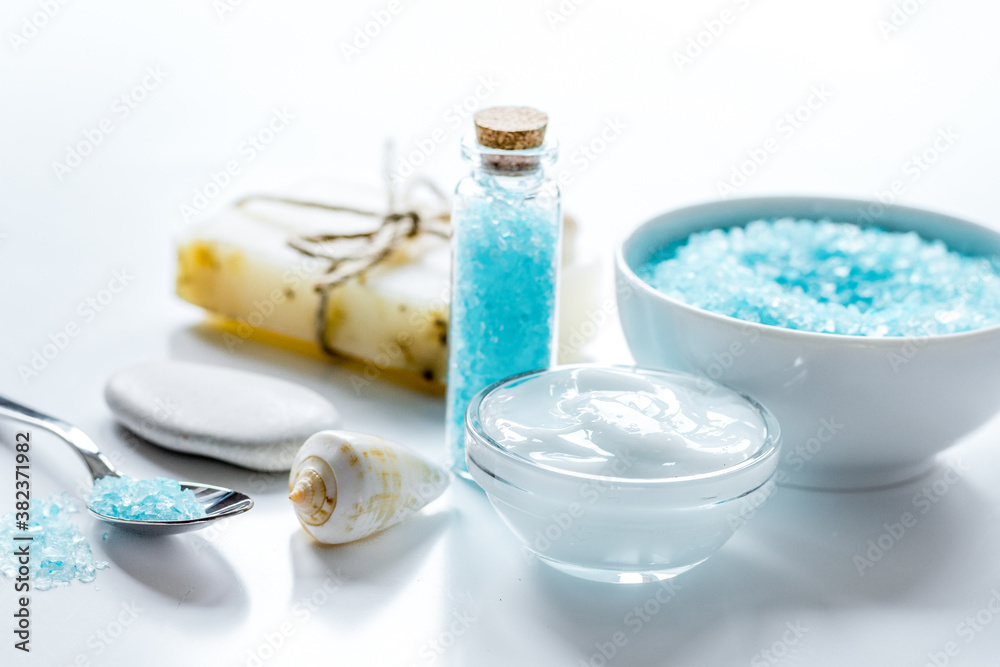 blue bath salt, body cream and shells for spa on white table background