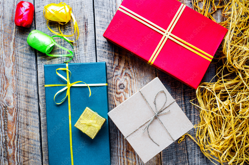 Colored gift boxes on wooden background with ribbon and straw