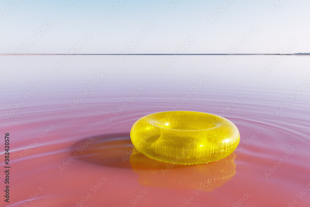 Bright yellow inflatable ring float in pink water lake. Creative color background