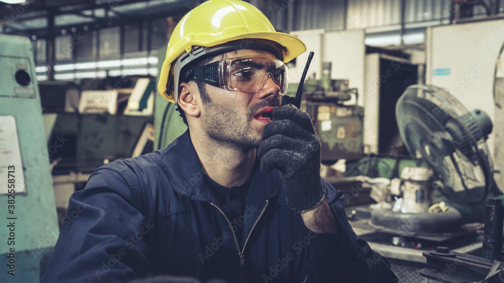 Factory worker talking on portable radio while inspecting machinery parts . Industrial and engineeri