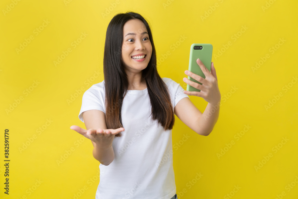 Beautiful Asian woman. She feels shocked with the phone on a yellow background.