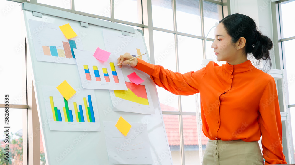 Young woman explains business data on white board in casual office room . The confident Asian busine