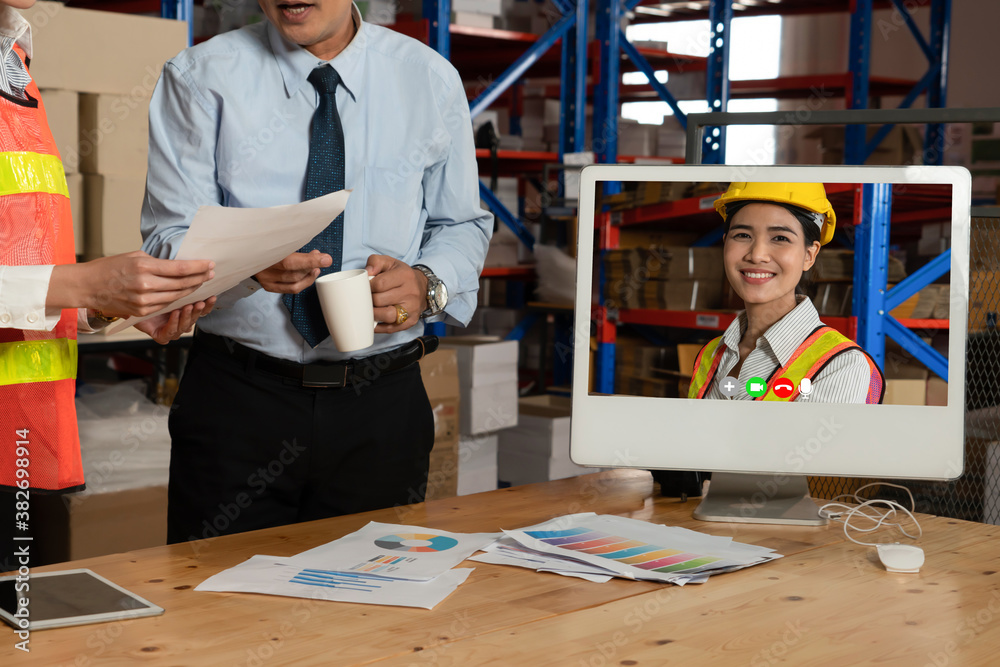 Warehouse staff talking on video call at computer screen in storage warehouse . Online software tech