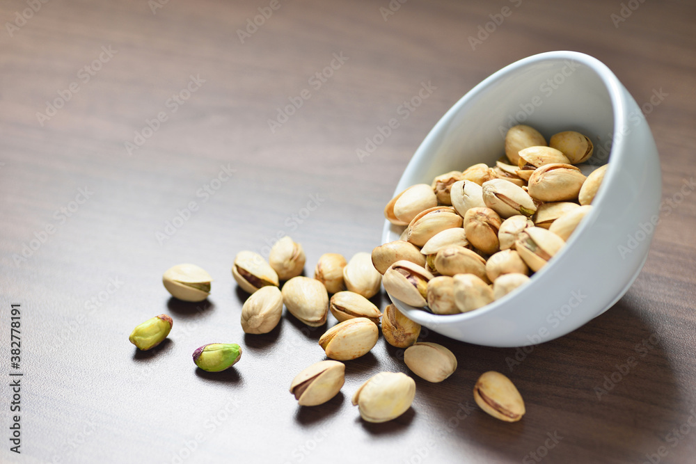 Close-up Pistachio nuts with white bowl on wooden background