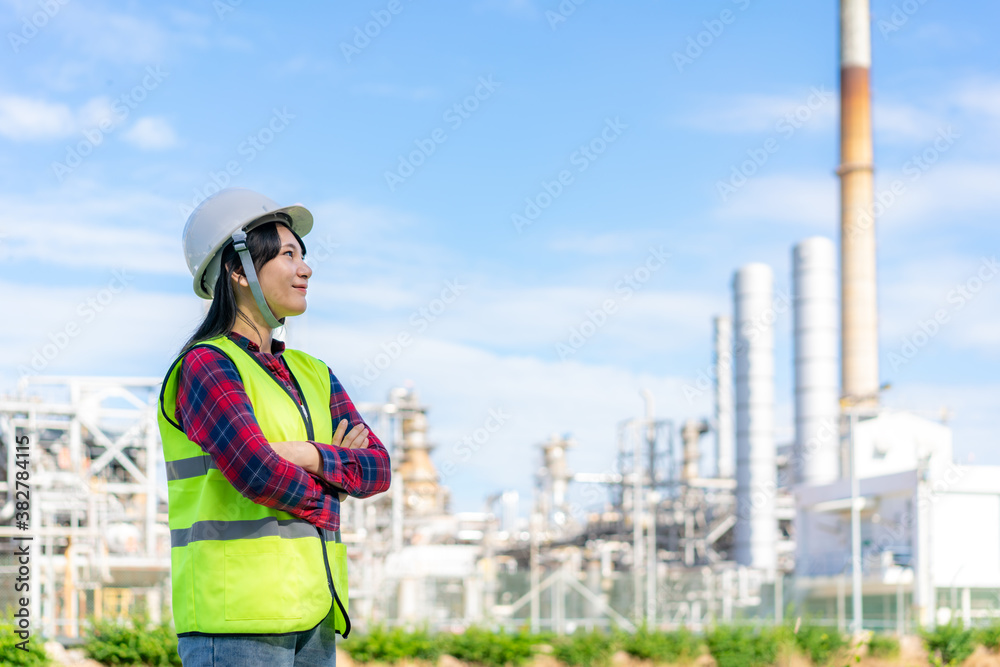 Asian woman engineer arm crossed with confident looking forward to future with oil refinery plant fa