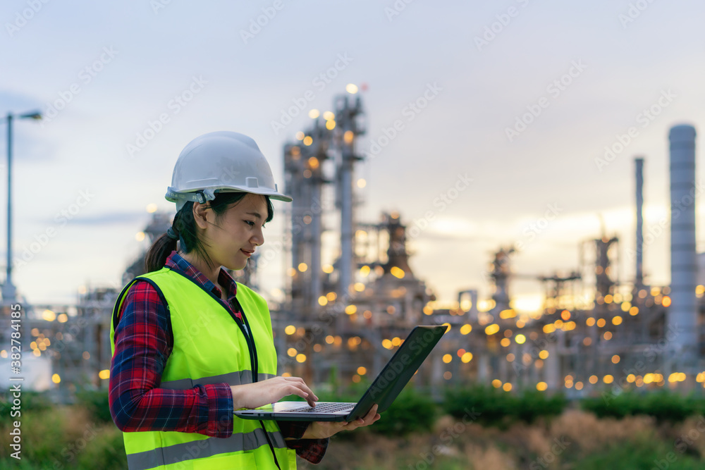 Asian woman petrochemical engineer working at night with notebook Inside oil and gas refinery plant 