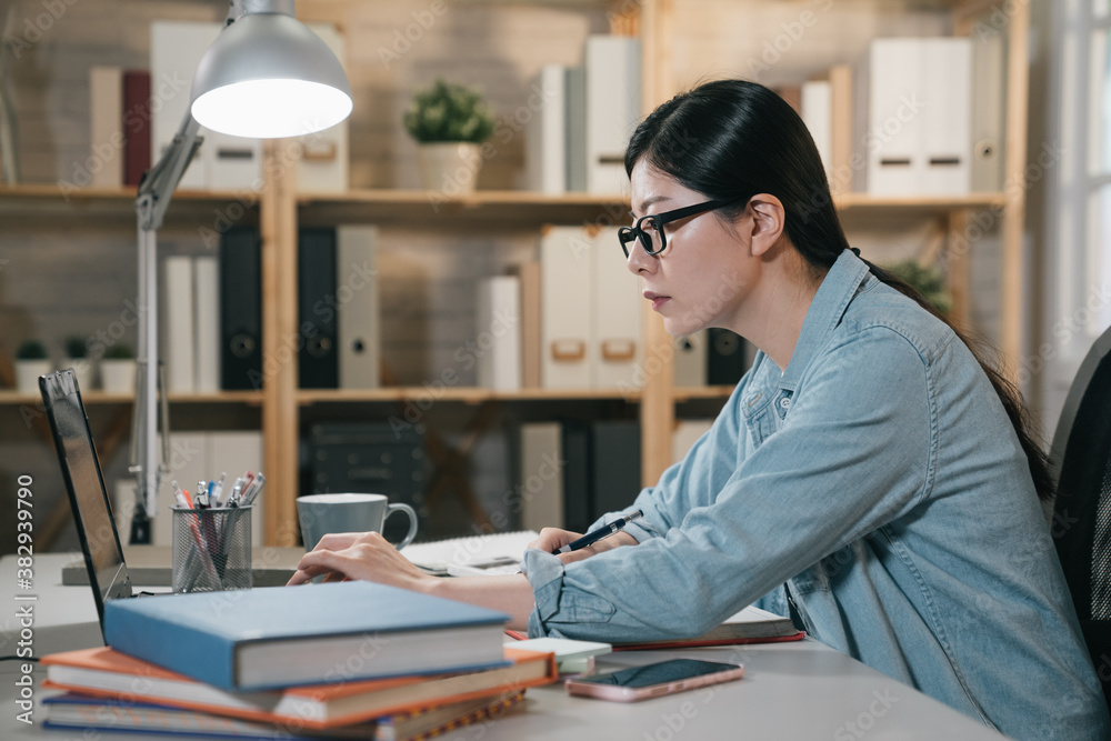 Indoor side view portrait of smart busy asian japanese woman making notes while sitting at home with