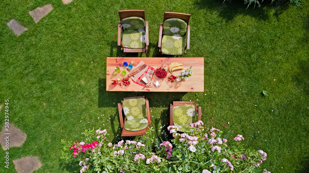 Decorated table with cheese, strawberry and fruits in beautiful summer rose garden, aerial top view 