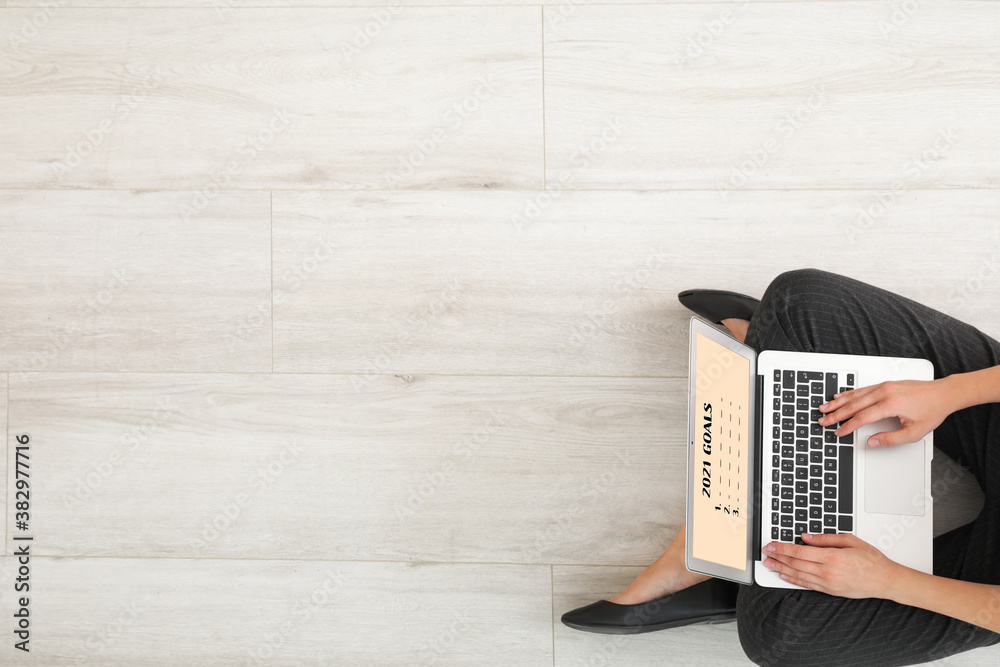 Young woman with laptop making to do list on 2021 year at home