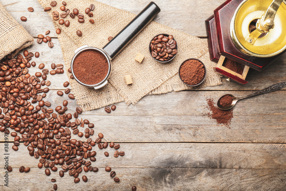 Portafilter with coffee powder, beans and grinder on wooden background