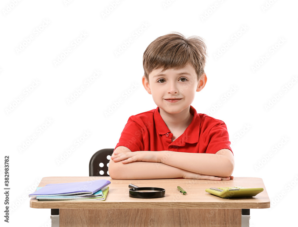 Little pupil sitting at school desk against white background