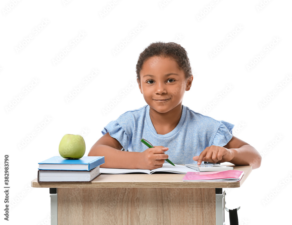 Little African-American pupil sitting at school desk against white background