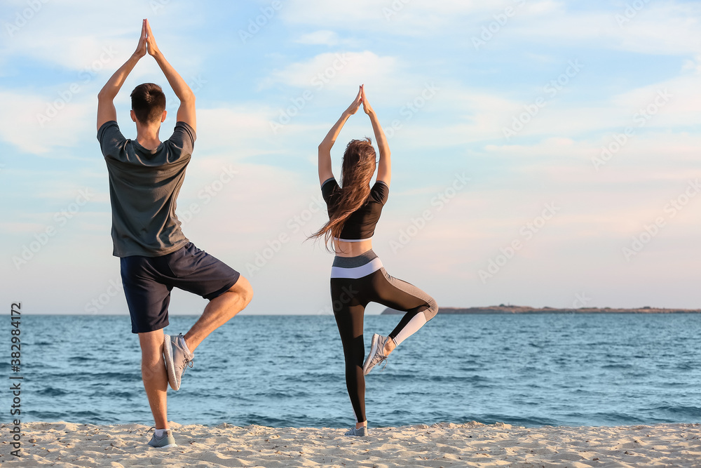 Sporty young couple practicing yoga on sea beach