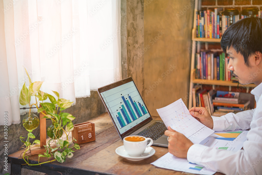 A man was working from home with a laptop ,paper sheet while  watching the graph statistic on the co