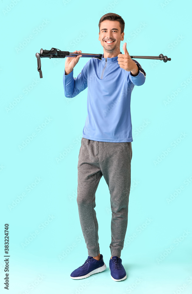 Young man with walking poles showing thumb-up on color background